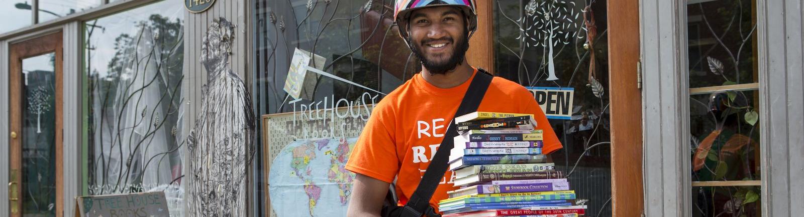 man carrying a tall stack of books on his bike