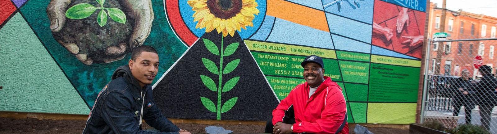 two men sitting in front of a mural on Bouvier Street